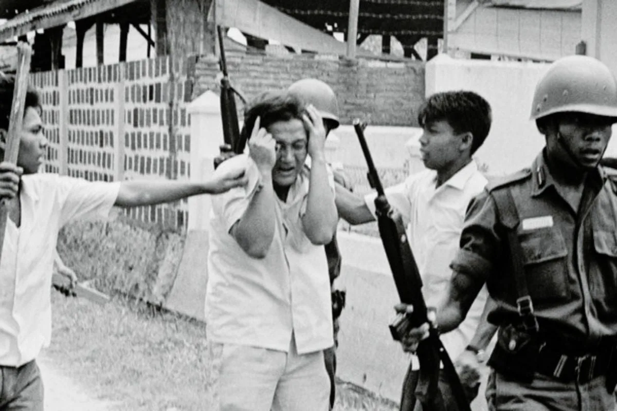 Archival photograph: armed men and a soldier seize a man who clutches his head.